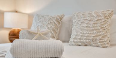 Cozy white bed with textured pillows and a folded towel topped with a starfish.