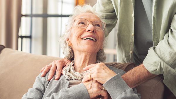 Elderly woman smiling while holding hands with a younger person.
