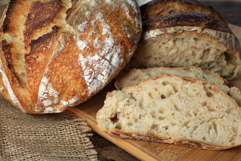 Sourdough bread and slices, fresh from the oven, with a crispy, smoky top and a side of starter