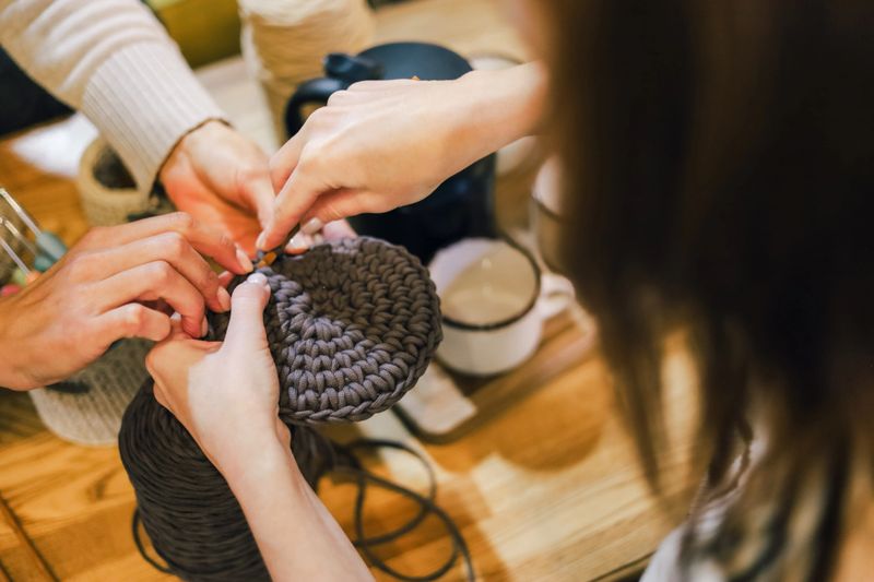 Close-up of hands working together on a round crochet piece with thick yarn, capturing a warm, creative, handmade crafting moment ideal for hobby, artisan, or DIY themes.