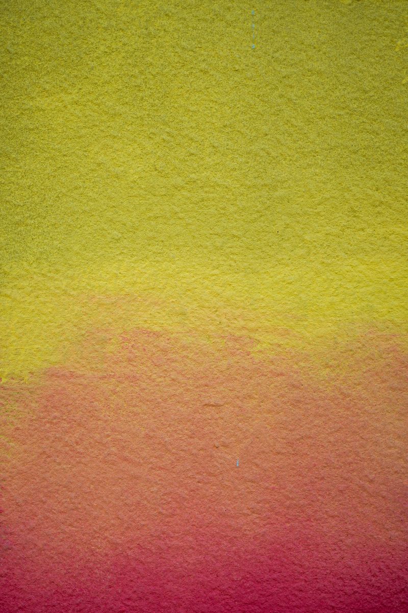 A close-up view of a wall with a colorful gradient from yellow to pink, showcasing a textured surface.