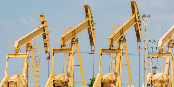Three yellow oil pump jacks under a blue sky.