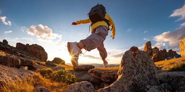 Person hiking and jumping on rocky terrain at sunset.