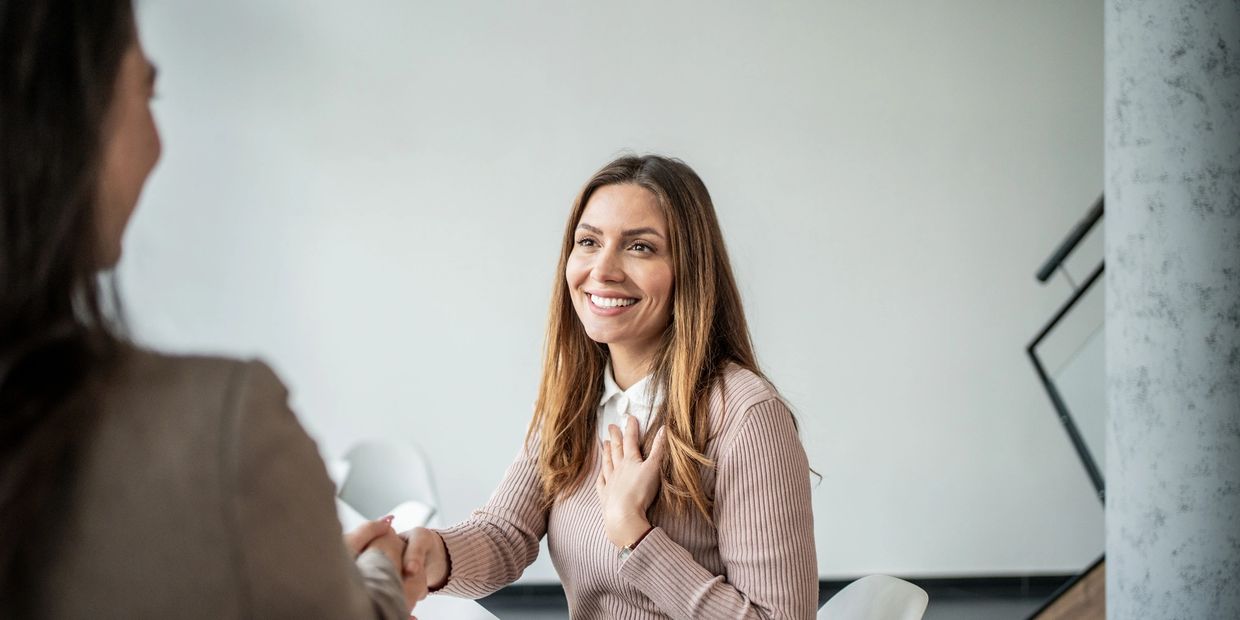 Woman smiling and shaking hands with another person.
