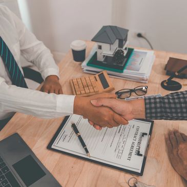 Two people shaking hands over a signed construction contract on a wooden desk.