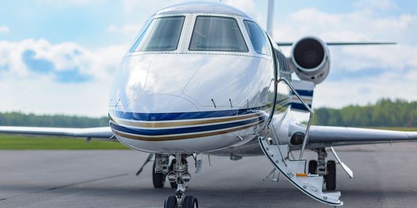 A private jet with open stairs on the runway under a partly cloudy sky.