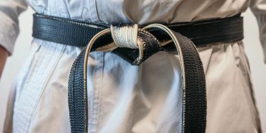 Person ties a black belt in a martial arts uniform.