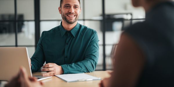 A smiling professional seated at a laptop during an office meeting.