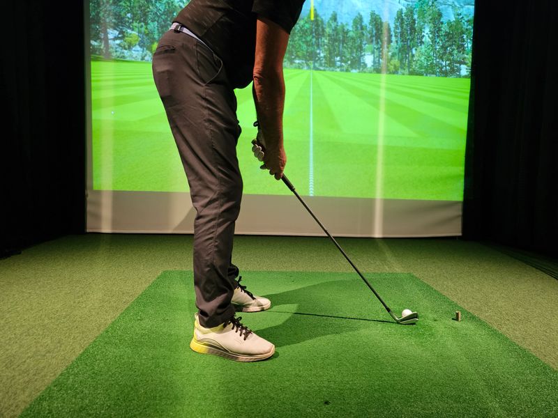 Golf player practicing swing at indoor simulator with realistic screen