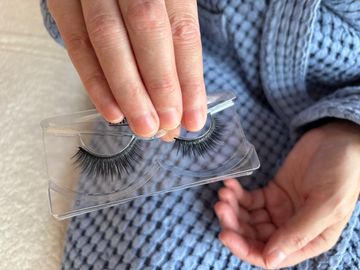Hand holding a pair of false eyelashes in plastic packaging.