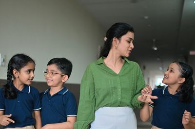 Teacher walking and talking with happy schoolchildren in uniform.