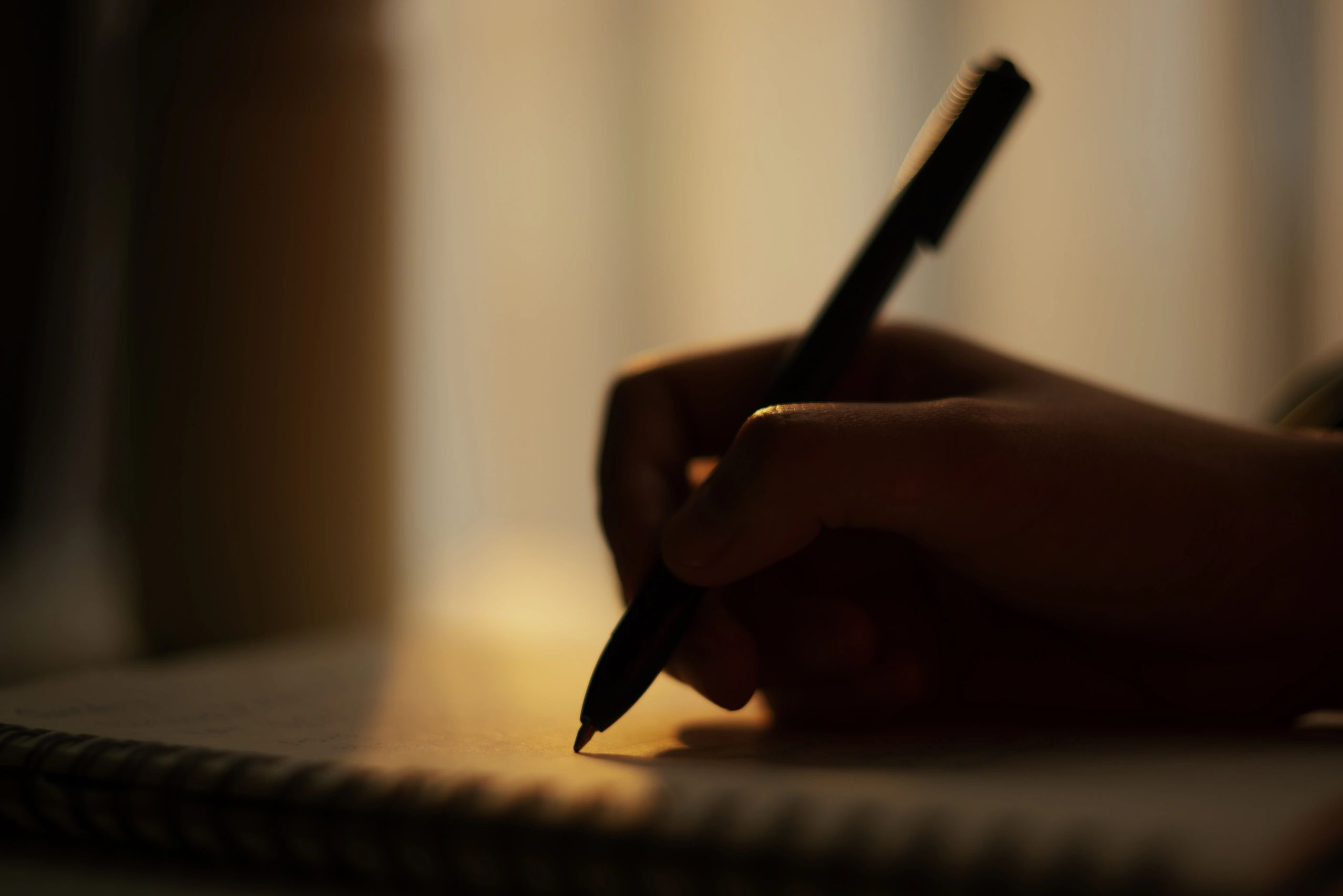 Silhouette of a hand writing in a notebook with warm lighting.