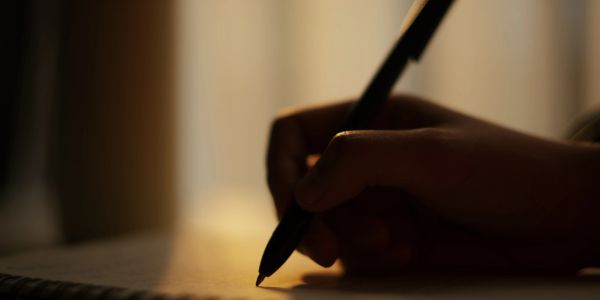 Hand holding a pen, writing in soft warm light.