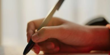 A hand holding a pen, writing on paper.