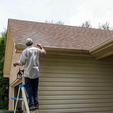 Man inspecting or repairing house gutters on a ladder.