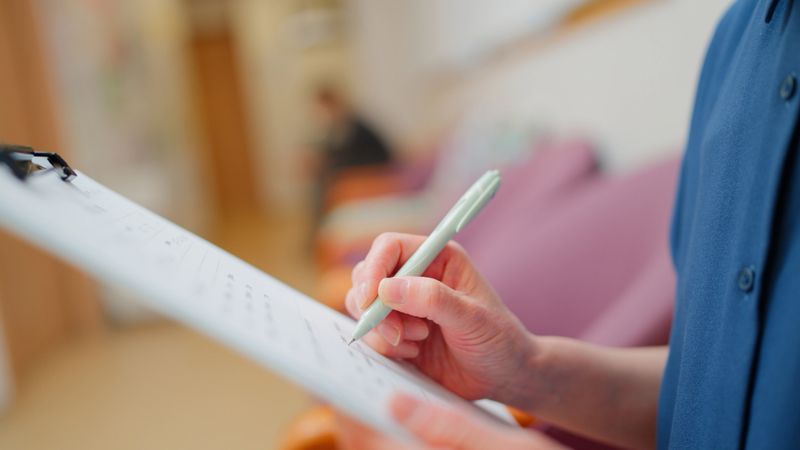 A senior adult female patient is filling in the medical questionnaire while waiting for her turn in a clinic.