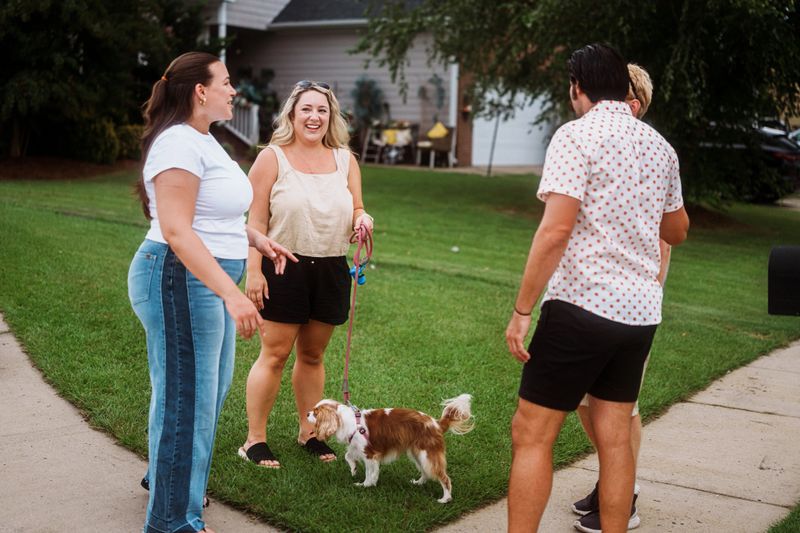 A cheerful group of neighbors shares stories and laughter right outside their homes along the sidewalk during a casual weekend hangout.
