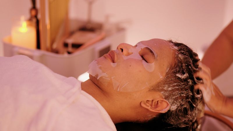 Male client relaxing deeply in the salon, experiencing a dual treatment of a cleansing hair wash and a nourishing facial mask.