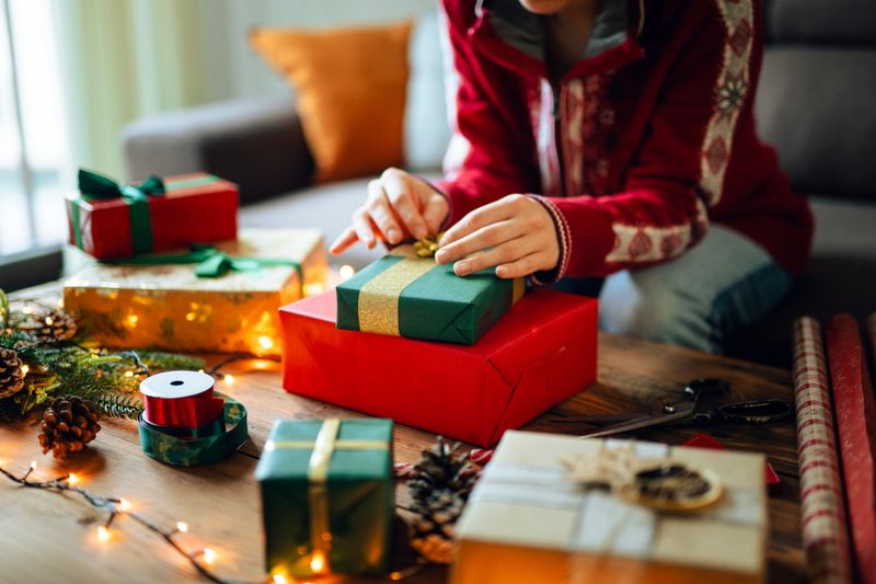 Shot of unrecognizable woman wrapping and decorating Christmas presents with themed paper and ribbons.