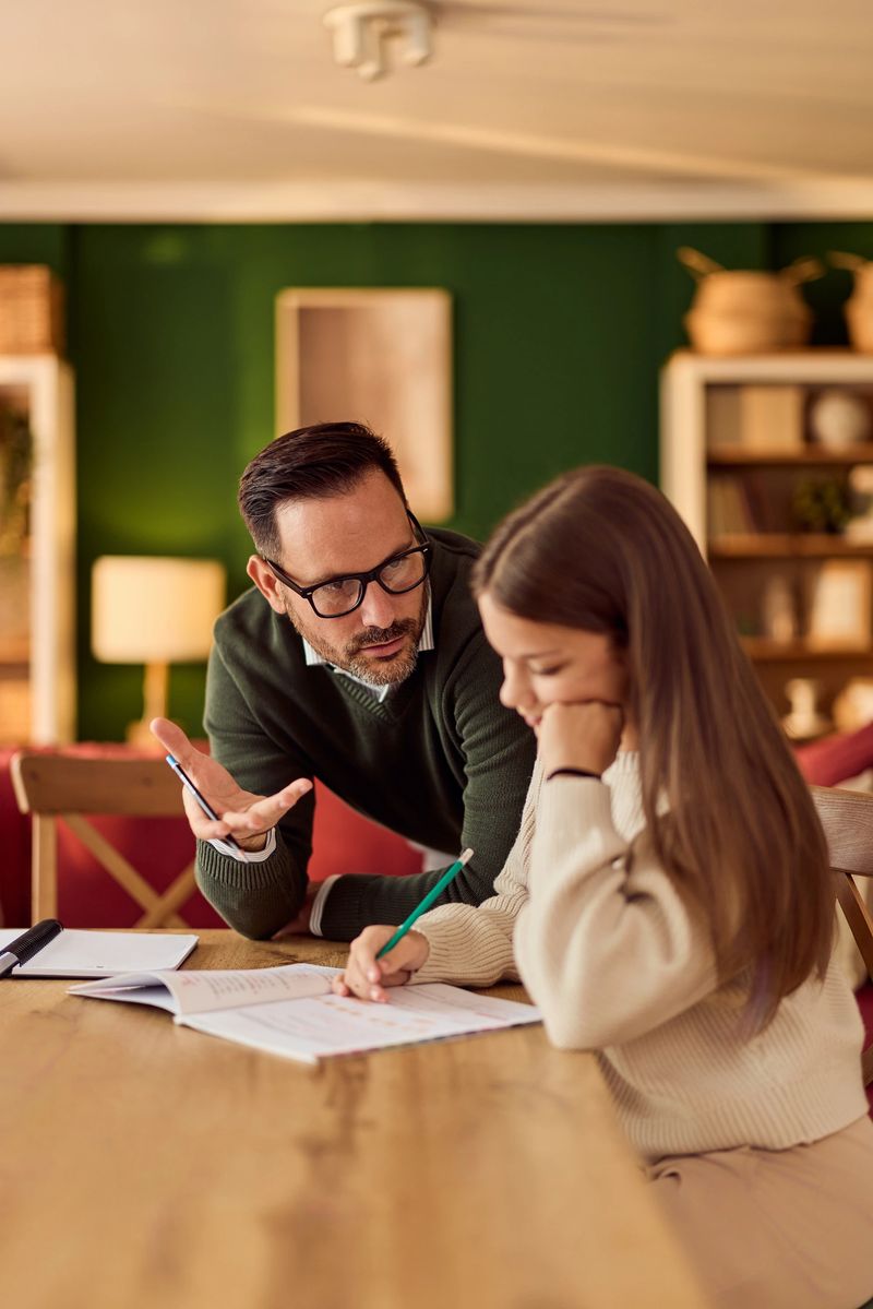 A father assists his daughter with homework in a warm, inviting living room study setup.