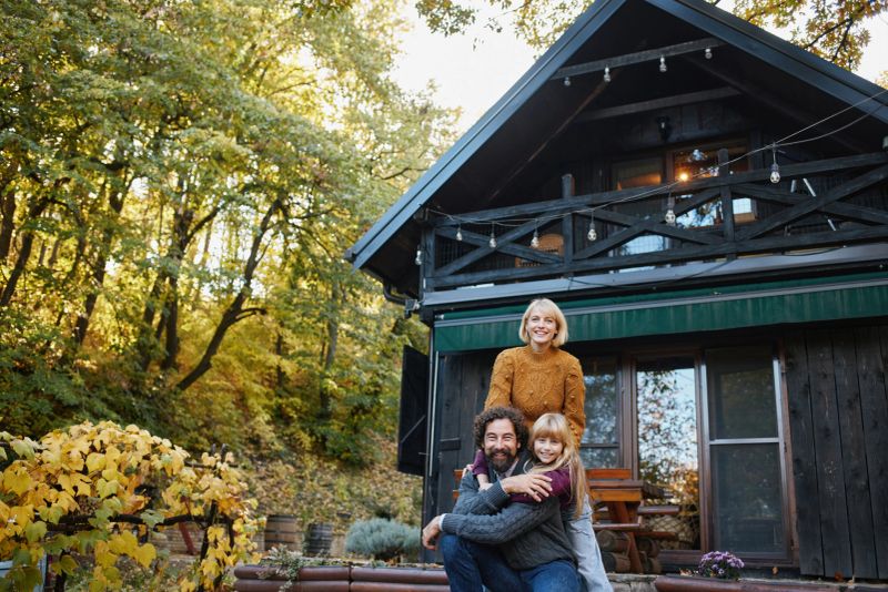 Family is enjoying and posing in front of a cozy cabin during an autumn weekend