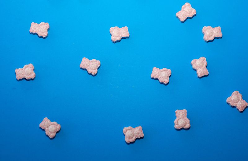 This is a colorful studio shot of pink, gummy vitamins shaped like bears, scattered randomly on a saturated, bright blue background.