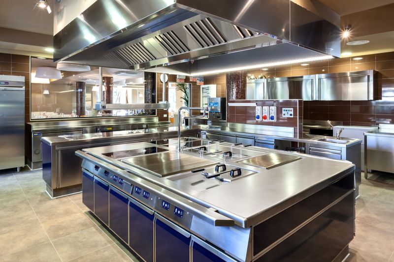 Modern industrial kitchen with induction island, sinks, ventilation hood, and stainless appliancesideal for culinary operations.