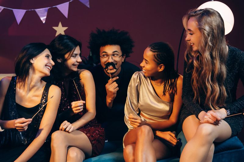 Young adults enjoying a fun party together, posing with playful photo booth props and smiling