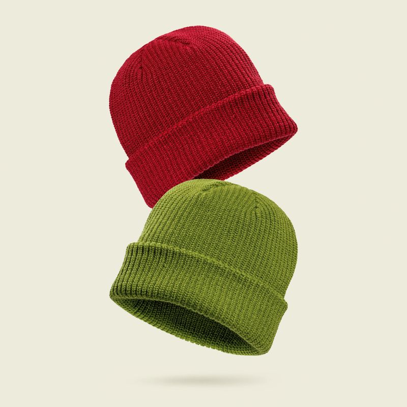 Red and green knitted beanie hats floating on light beige background. Concept of modern warm winter accessories, cozy seasonal fashion, colorful casual style for cold weather and urban lifestyle