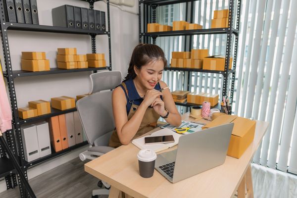 Woman working on packaging orders with a laptop in a cozy office.