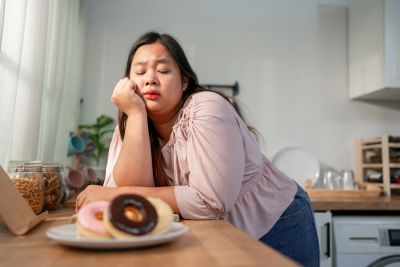 Woman looking tired or bored near donuts in kitchen.