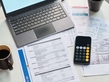 Workspace with laptop, documents, calculator, and coffee.