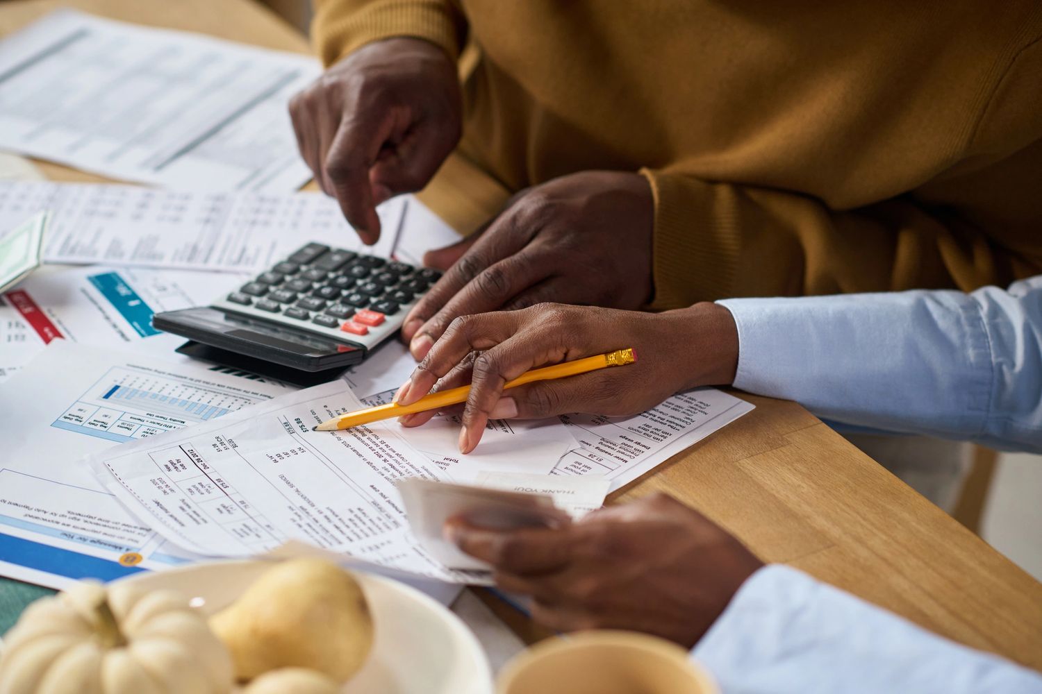 Two people calculating bills with a calculator and pencil at a wooden table.