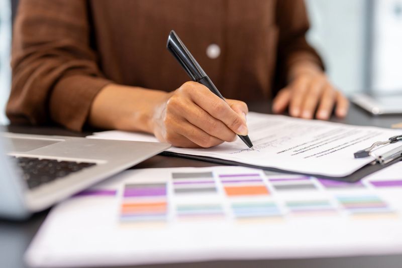 Businesswoman's hand holding a pen and signing a contract, an official paper document, sealing an agreement, deal, or important transaction in an office setting