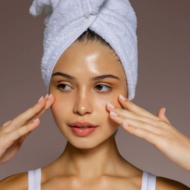 Woman with a towel wrapped around her head touching her face gently.