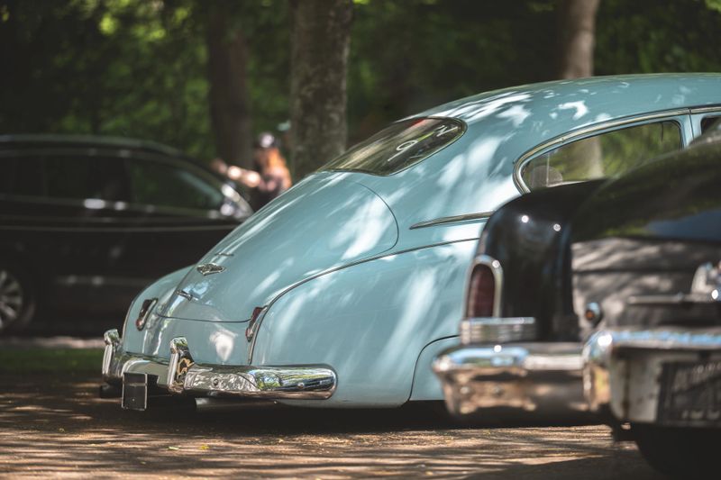 This image captures the rear of a vintage light blue car, showcasing its classic design and chrome accents