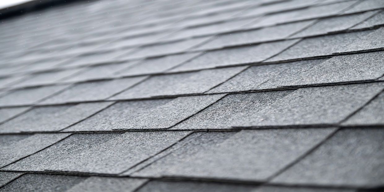 Close-up of gray asphalt roof shingles during light rain.