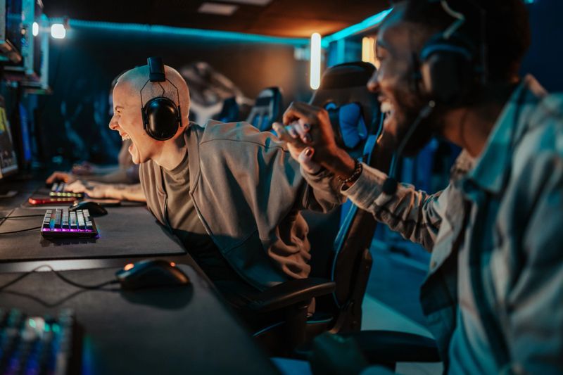 Two young adult gamers high-fiving, celebrating a win in a vibrant, neon-lit internet cafe or esports competition