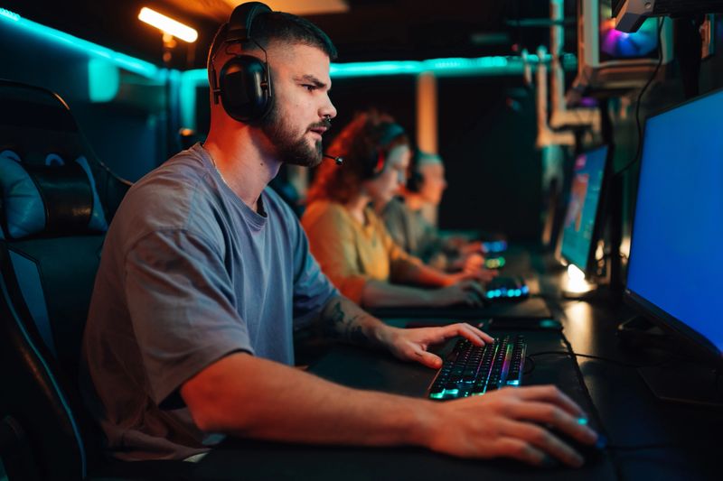 Young man intensely focused playing competitive esports under neon lights in a packed arena, headset on, keyboard and mouse in hand