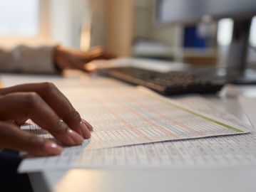 Hands reviewing printed spreadsheets on a desk.