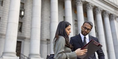 Dos profesionales revisan documentos frente a un edificio institucional.