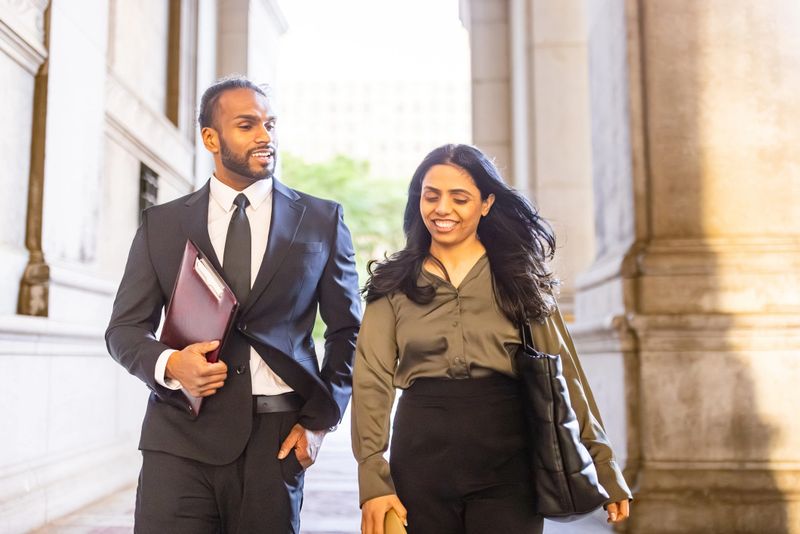 Two business professionals walking confidently outdoors together. Man in suit and woman in professional attire, smiling and engaged in conversation.