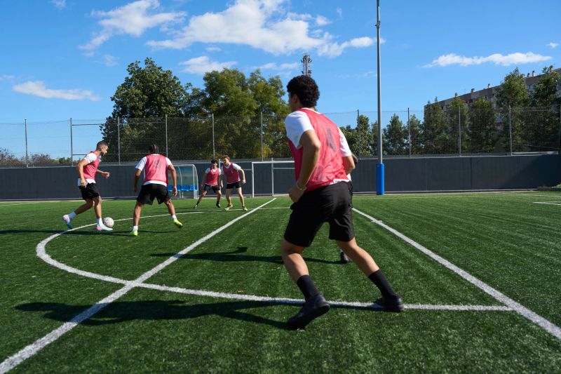 Adult men training in football on a sunny pitch, practicing drills and teamwork to build skill, fitness, agility and camaraderie