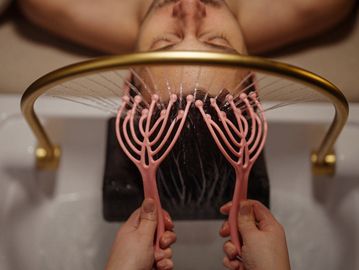 Person receiving a scalp massage with water and scalp brushes.
