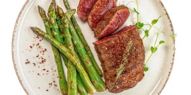 Grilled steak and asparagus garnished with herbs on a white plate.