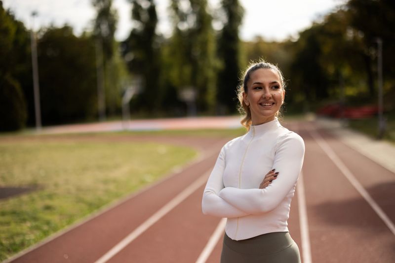 Portrait of smiling young coach in active wear standing on treadmill in park.