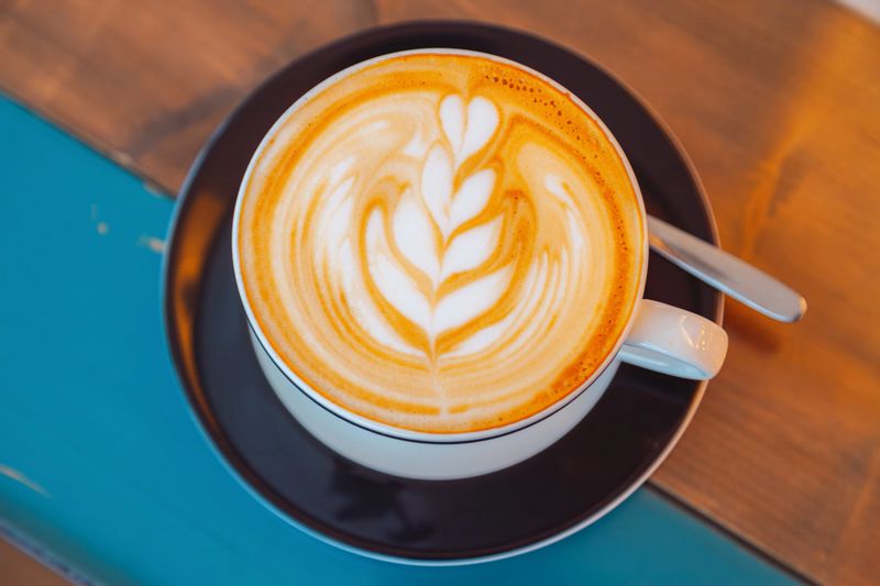 A beautifully crafted artisan latte served in a stylish ceramic cup, featuring smooth creamy microfoam and elegant latte art, captured in a warm and inviting café atmosphere with natural light and wooden textures enhancing the cozy coffeehouse mood