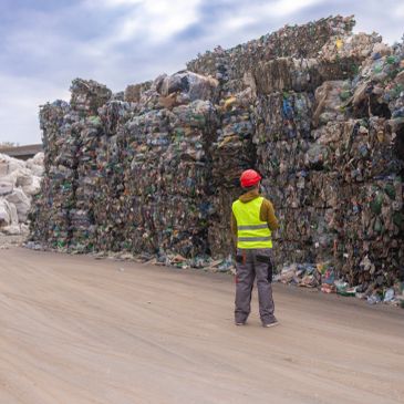 Trabajador observa grandes fardos de basura reciclada.
