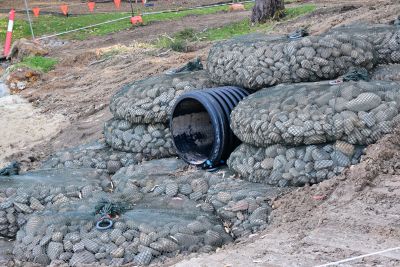 Rock-filled gabion baskets with drainage pipe on construction site.