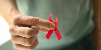 Hand holding a red awareness ribbon.